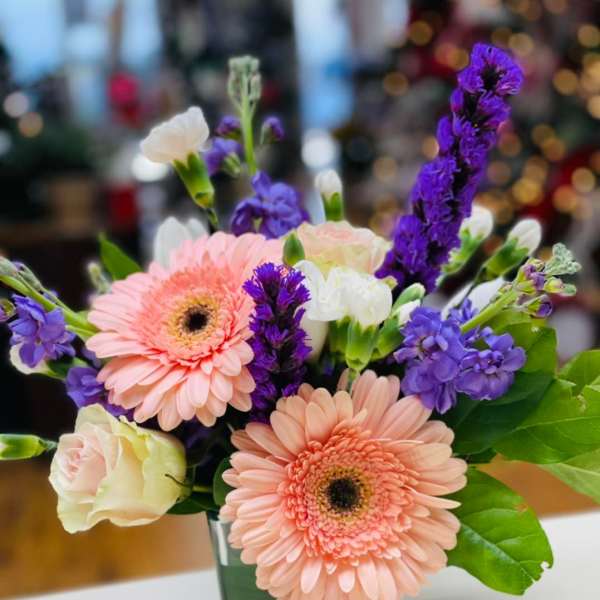 Pink gerbera daisies and purple flowers in a glass vase