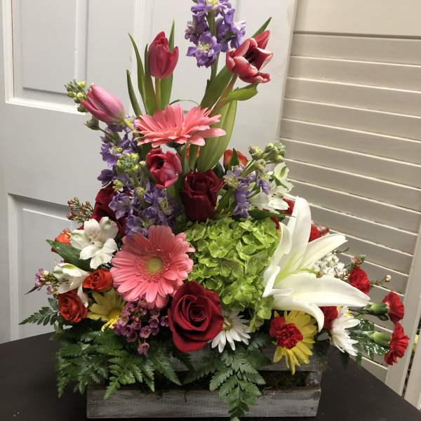 Colorful mixed flower arrangement in a wooden box with lilies and roses