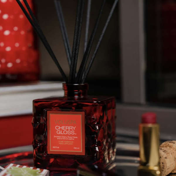 Red reed diffuser bottle with black sticks and a cherry gloss label