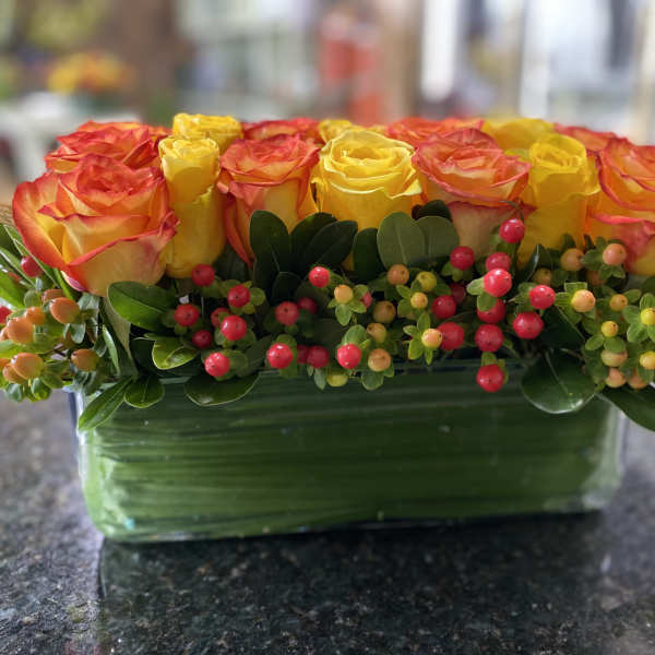 Yellow and orange roses in a rectangular glass vase with berry accents