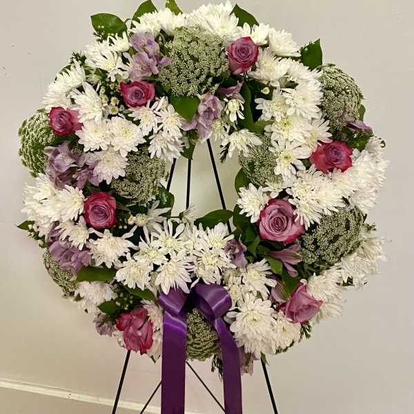 Round floral wreath with white daisies, pink roses, and a purple ribbon