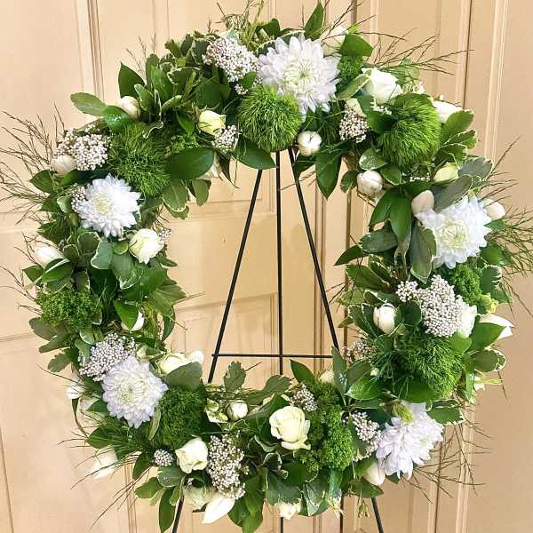 Standing wreath of white flowers and green accents on a metal easel