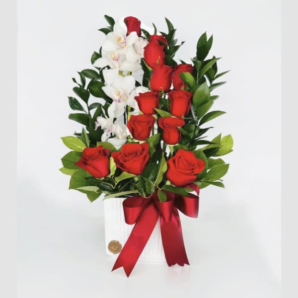 Red roses and white orchids arranged in a white vase with a red ribbon