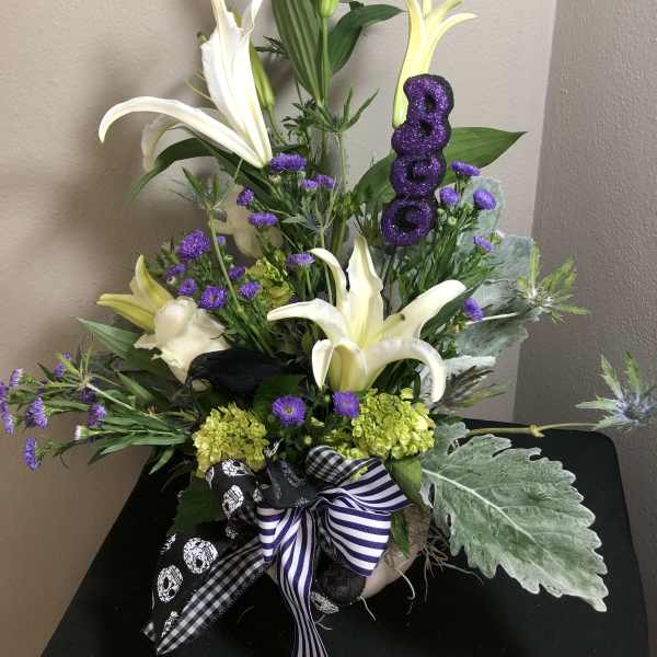 White lilies and purple flowers in a vase with a glittery purple "BOO" pick