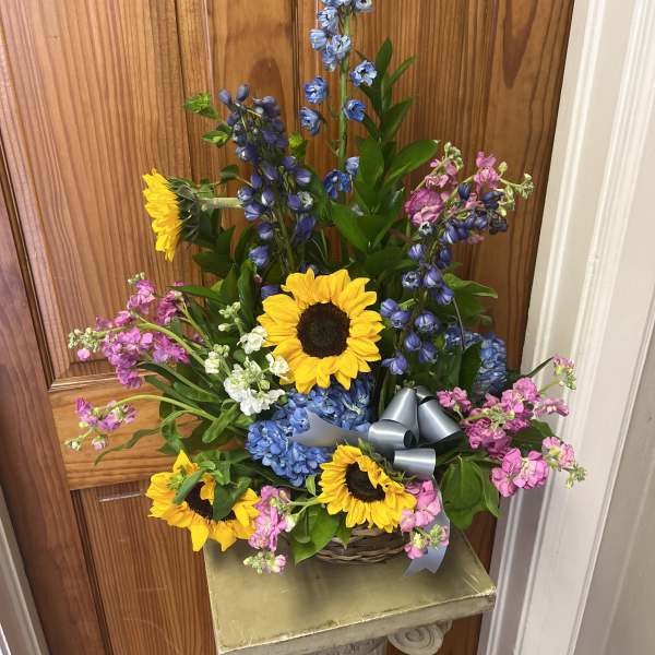 Tall mixed flower arrangement with sunflowers, blue blooms, and pink flowers in a basket
