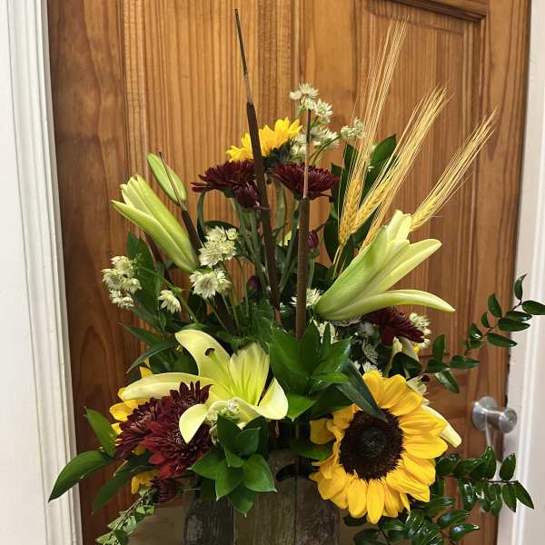 Tall mixed flower arrangement with sunflowers, lilies, and dark mums in a rustic vase