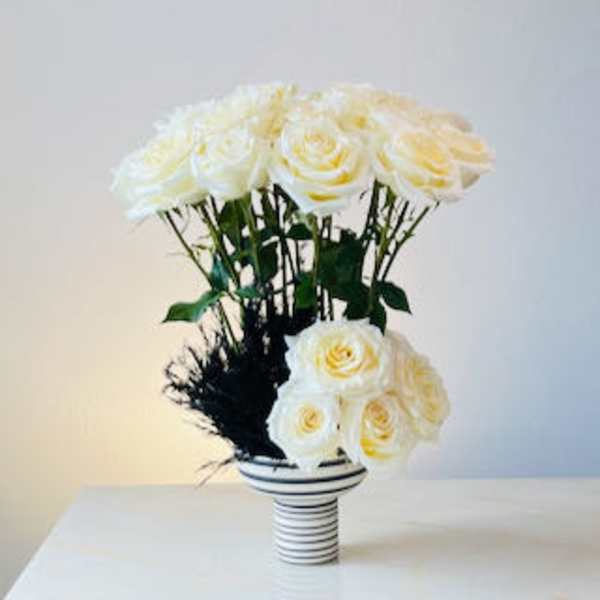 White roses arranged in a striped vase with dark foliage