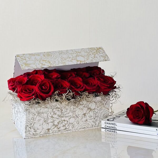 Box of red roses with one rose beside a stack of Chanel books