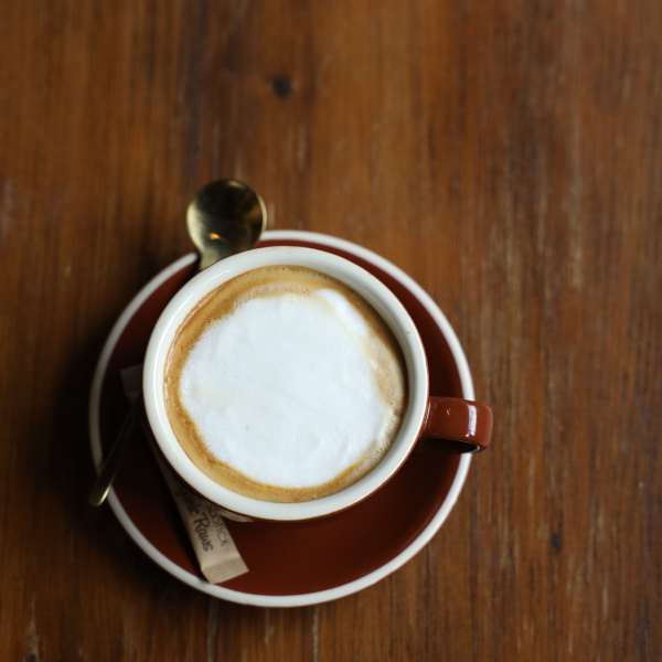 Cup of cappuccino on a saucer with a spoon on a wooden table