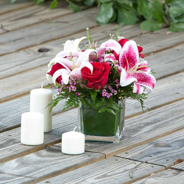 Red roses and pink lilies in a square glass vase with white candles