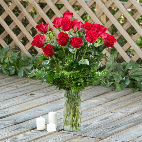 Red roses in a clear glass vase with three white candles nearby