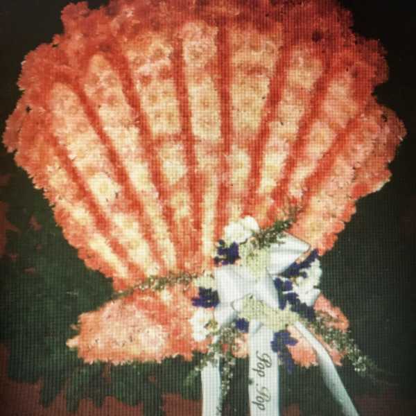 Orange carnation standing spray with white ribbon and blue accents