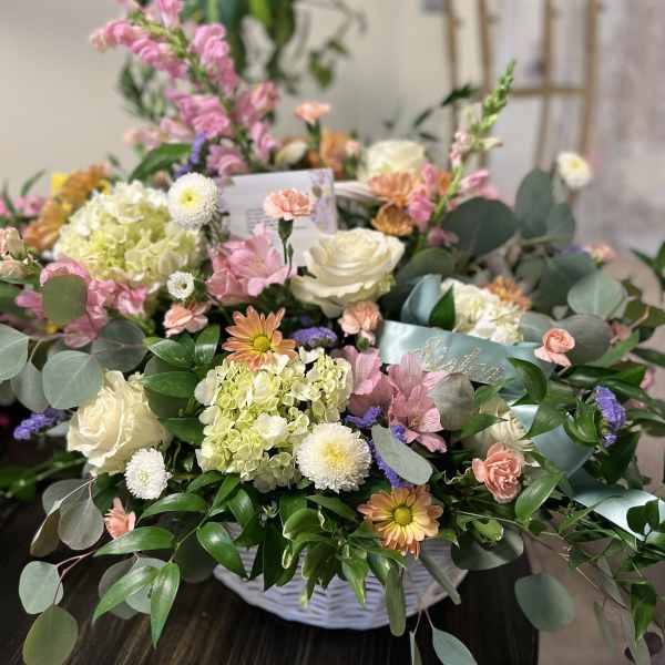 Mixed pastel flower arrangement in a white basket with roses and chrysanthemums