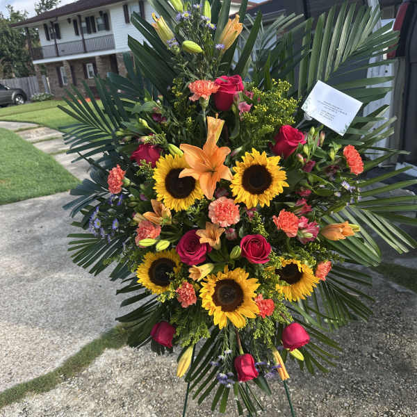 Standing floral spray with sunflowers, roses, lilies, and palm fronds