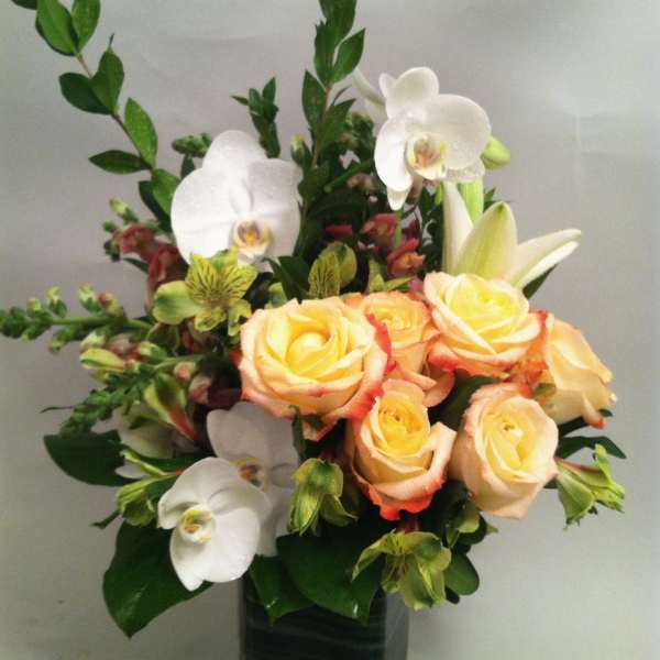 Peach roses with white orchids and lilies in a tall glass vase