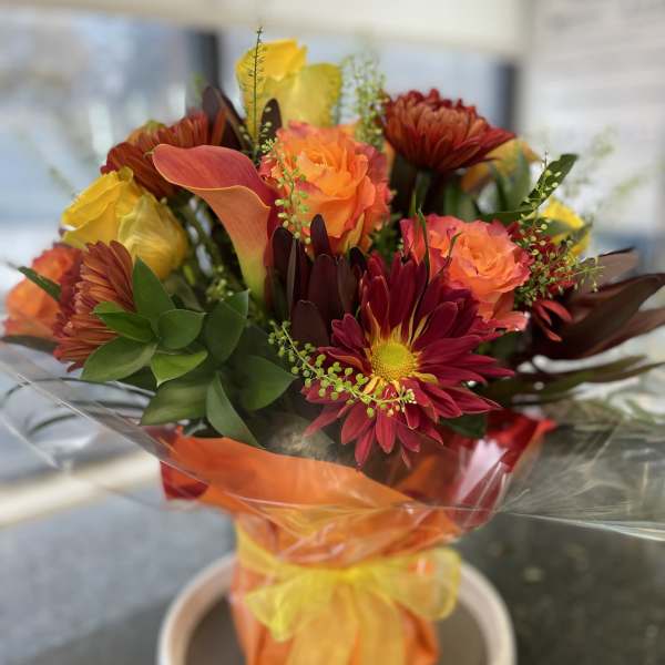 Bouquet of orange and red flowers wrapped in orange cellophane with a yellow ribbon