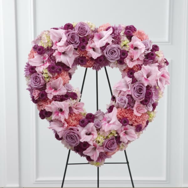 Heart-shaped floral wreath in pink and purple tones on a black stand