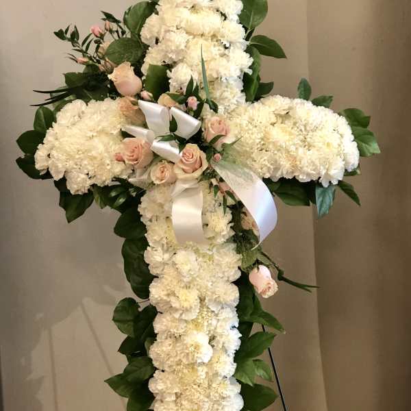 White floral cross on an easel with pink roses and ribbon