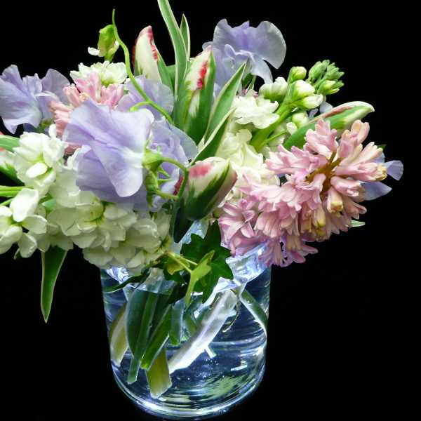 Small vase arrangement of pastel tulips, stock, hyacinth, and sweet peas on a black background