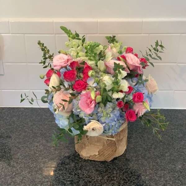 Mixed bouquet of pink roses, blue hydrangeas, and white blooms in a wrapped container