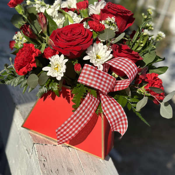 Red roses and white daisies in a red gift box with a gingham ribbon