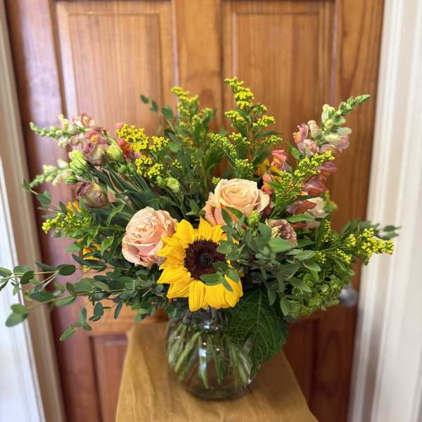 Mixed bouquet with sunflowers, blush roses, and yellow filler in a glass vase