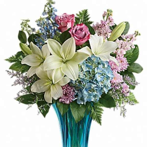 Bouquet of white lilies, pink roses, and blue hydrangeas in a blue glass vase