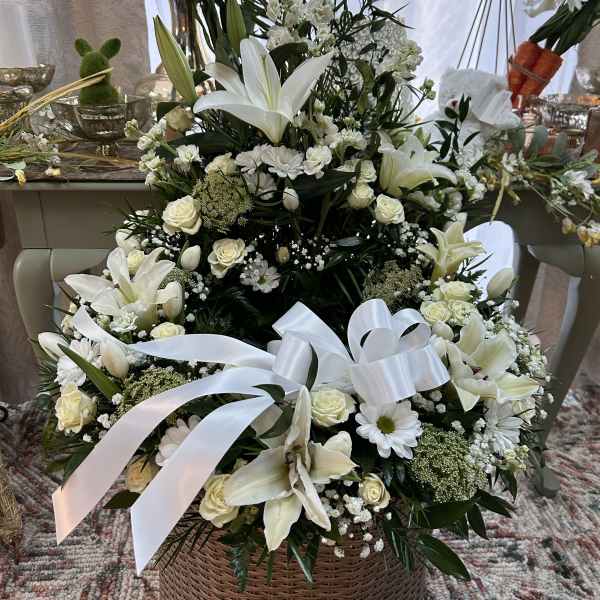 Tall white and cream lily and rose arrangement in a wicker basket with white ribbon bows
