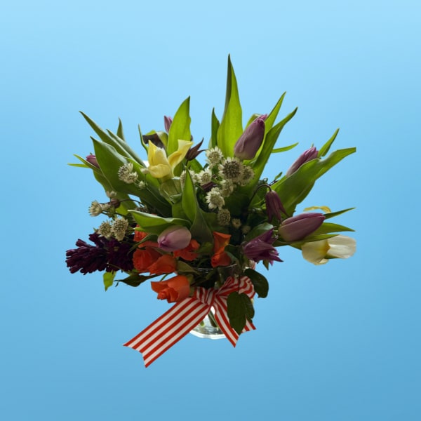 Mixed bouquet of tulips and other flowers in a glass vase with a striped ribbon
