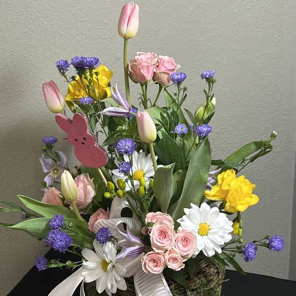 Mixed bouquet with pink tulips, roses, daisies, and purple filler in a moss basket