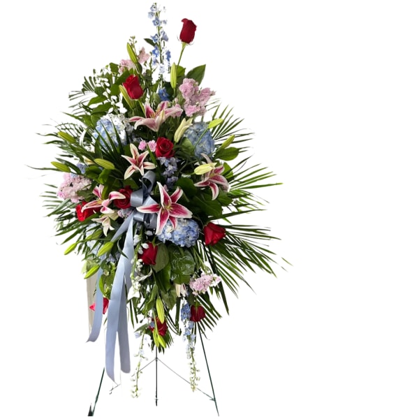 Tall standing floral spray with red roses, lilies, and blue flowers on an easel