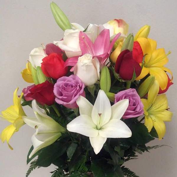 Mixed bouquet of lilies and roses in a glass vase with a red ribbon