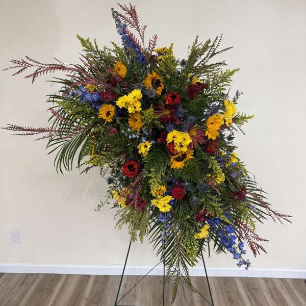Large standing floral spray with sunflowers, blue flowers, and mixed greenery
