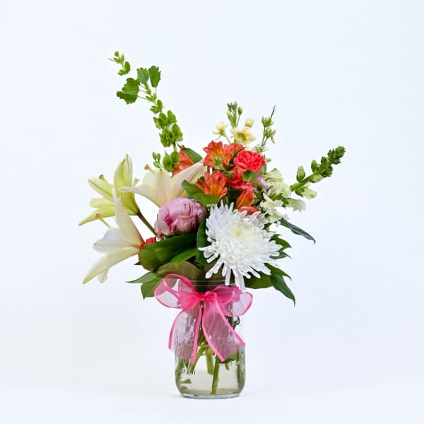 Mixed bouquet of lilies, chrysanthemums, and alstroemeria in a glass vase with a pink ribbon