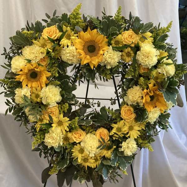 Heart-shaped floral wreath with yellow flowers on a black stand