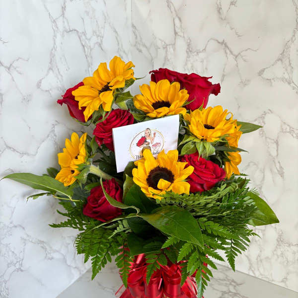 Bouquet of red roses and yellow sunflowers in a glass vase with a red ribbon