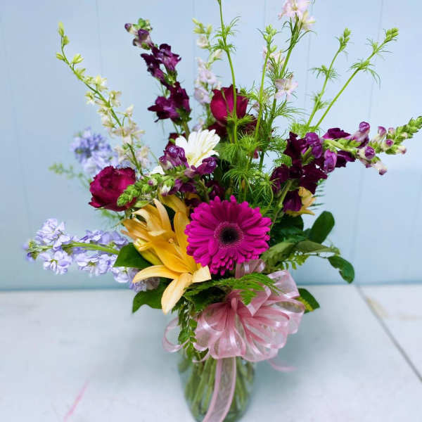 Mixed bouquet in a glass vase with pink ribbon and bright gerbera, lilies, and snapdragons
