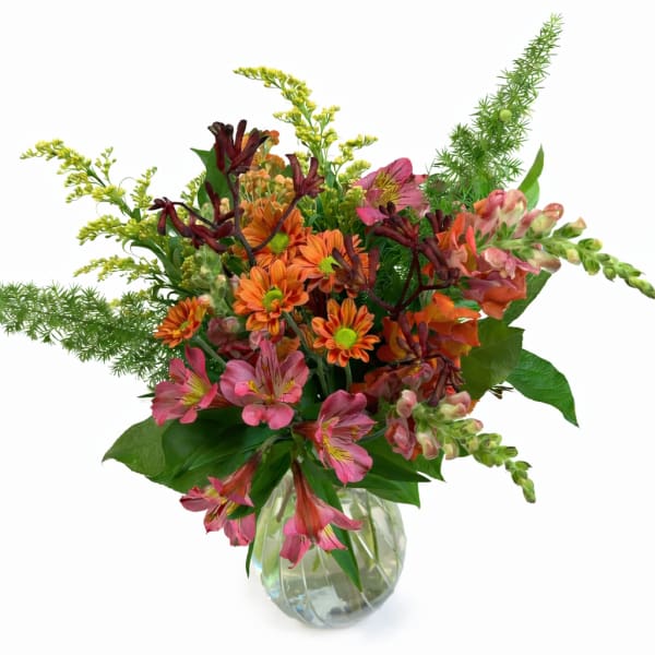 Mixed pink, orange, and burgundy flowers in a clear glass vase