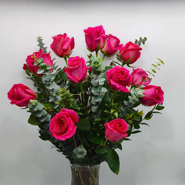Bright pink roses arranged in a clear glass vase with eucalyptus