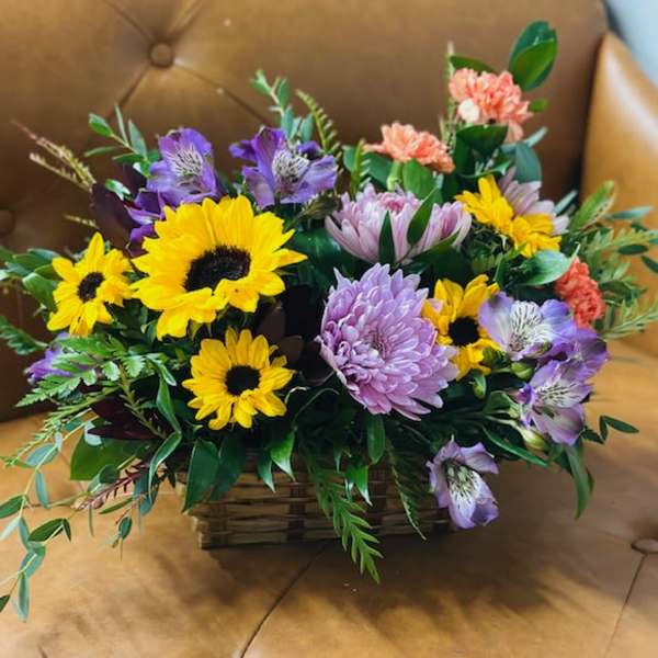 Mixed bouquet with sunflowers, purple blooms, and pink carnations in a basket