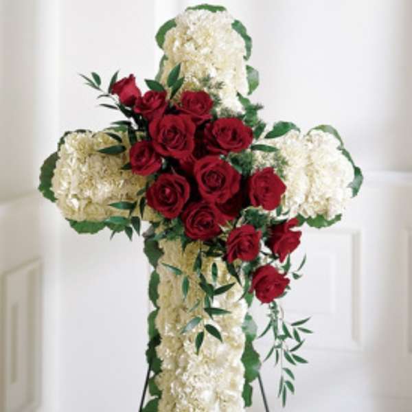 Cross-shaped floral tribute with red roses and white flowers on a stand