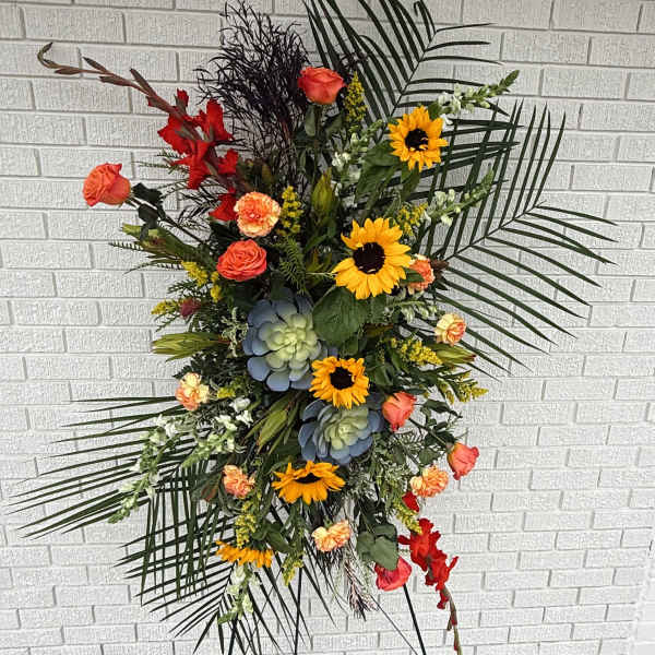 Tall floral spray with sunflowers, roses, and succulents against a brick wall