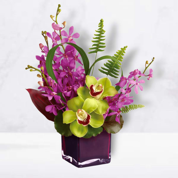 Purple orchids and green cymbidium orchids in a purple glass vase