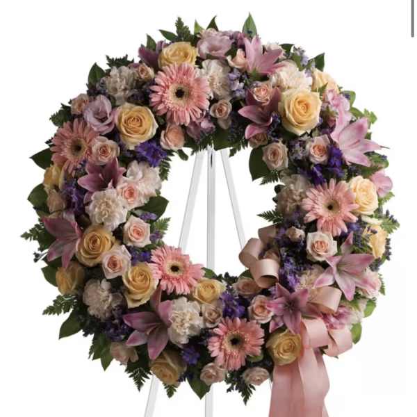 Large pastel floral wreath on a white stand with pink ribbon