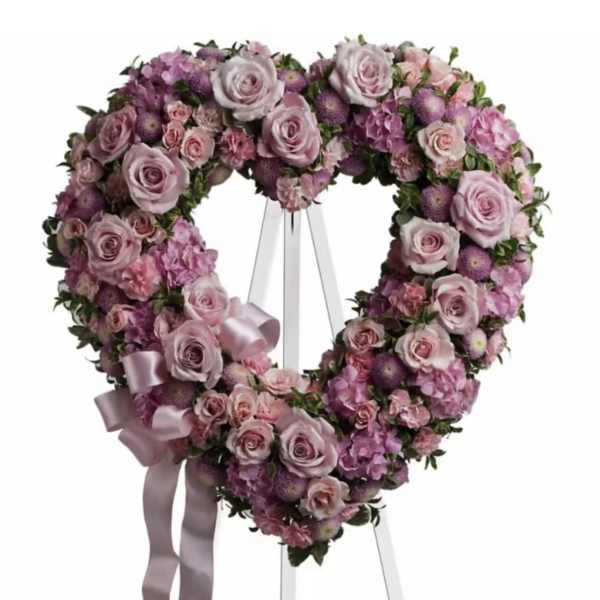 Heart-shaped floral wreath of pink and lavender roses on a white stand