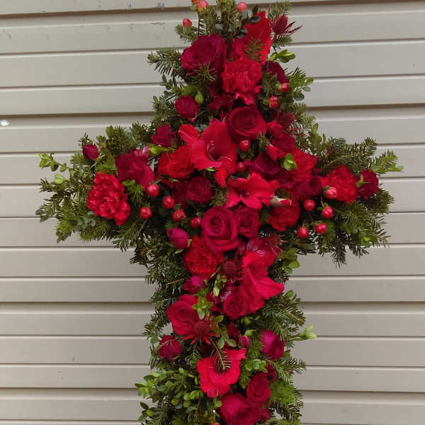 Cross-shaped floral spray with red roses and carnations on a stand