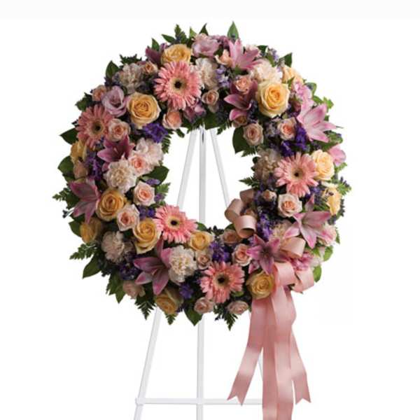 Pastel floral wreath on a white stand with a pink ribbon