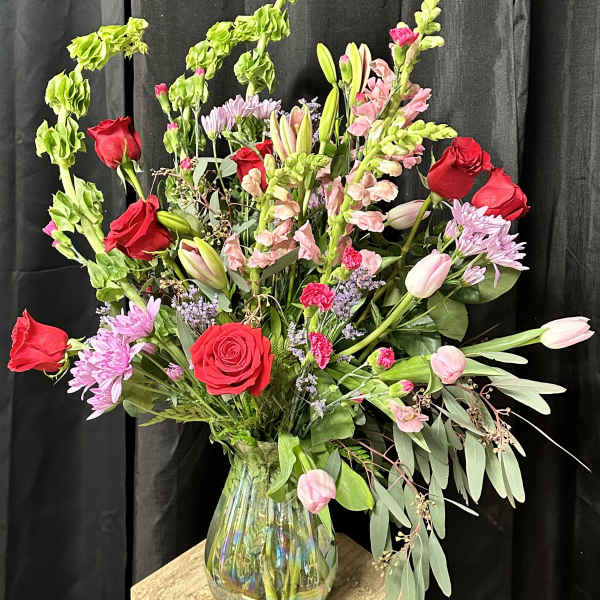 Mixed bouquet of red roses, pink tulips, and lilies in a glass vase