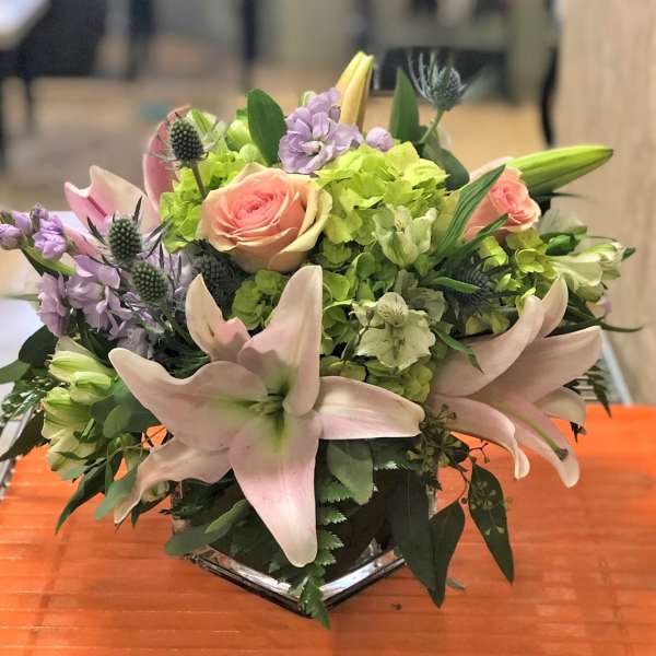 Low arrangement of pink lilies, roses, and green hydrangeas in a clear glass vase