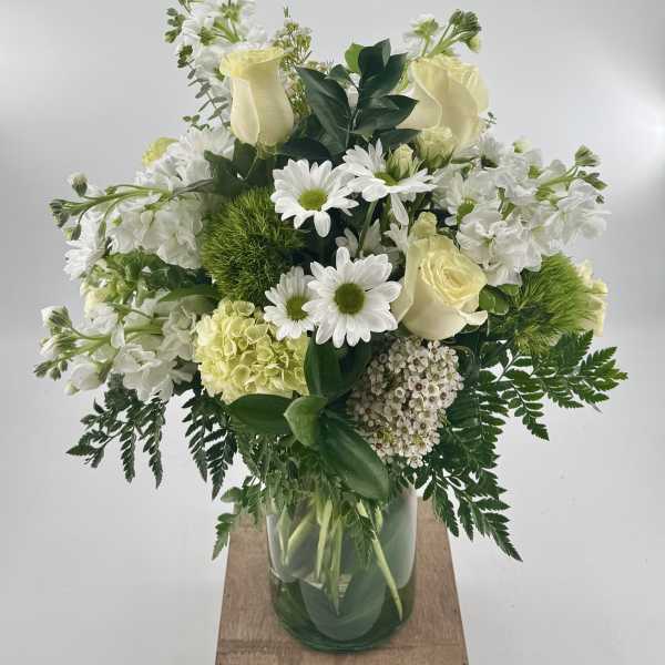 White and cream bouquet with roses, daisies, hydrangea, and green dianthus in a clear glass vase